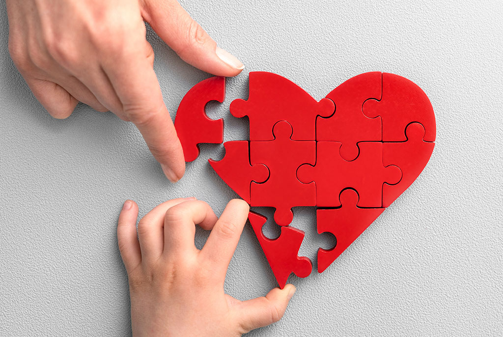 The concept of charity, love, donate and helping hand. International cardiology day. A woman and child arranges red heart shape puzzles. Symbol of helping others.